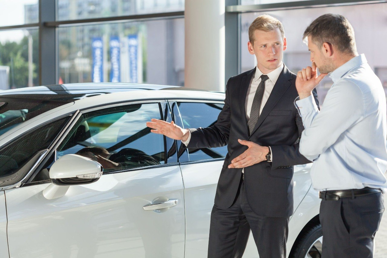 Vendedor mostrando um veículo branco a um cliente em concessionária